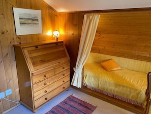 Ein Zimmer mit Holzboden, einem Bett, einem Schmuckkästchen, einem Gemälde und einer Lampe.