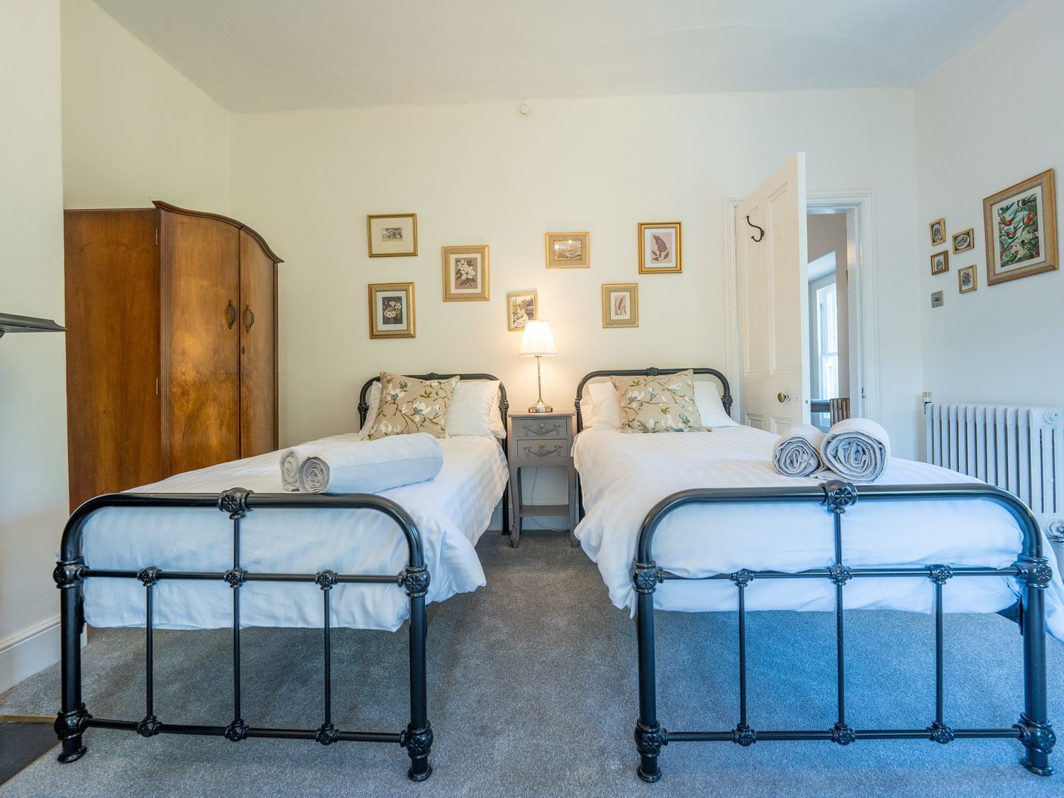 A double room with two beds, a wardrobe, bedside tables, a lamp, and framed pictures on the wall.
