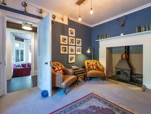 A room with a fireplace, leather armchairs, a patterned rug, and a wall adorned with framed pictures. - Gwynfryn House, Gorgeous Riverside Property Near The Beach (Llanbedr)