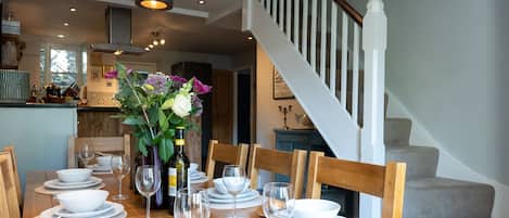 A dining table set for six with white plates, glasses, and cutlery. A vase with flowers is on the table.