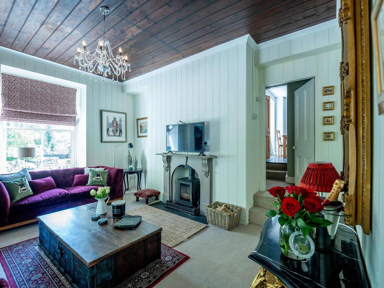 Una sala de estar con sofá, mesa de centro, chimenea, televisor y una araña.