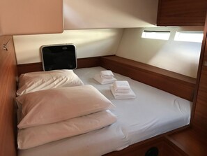 A small, neatly made bed with white linens and pillows, a smartphone on the headboard, and a window with natural light.
