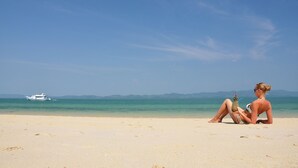 Una playa con un bote en el agua y una persona sentada en la arena.