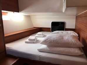 A small, compact bed with white linens and pillows, a smartphone charging station, and a wooden bench.