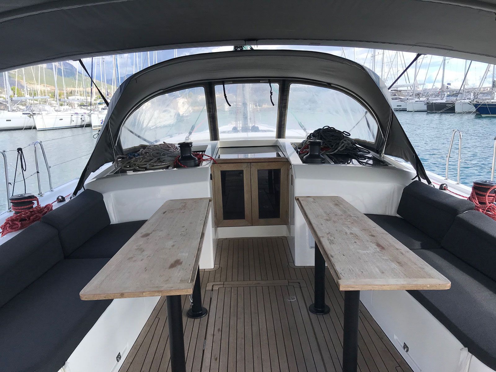 Le pont d’un bateau, avec une table centrale, des sièges rembourrés et une vue sur le port de plaisance.