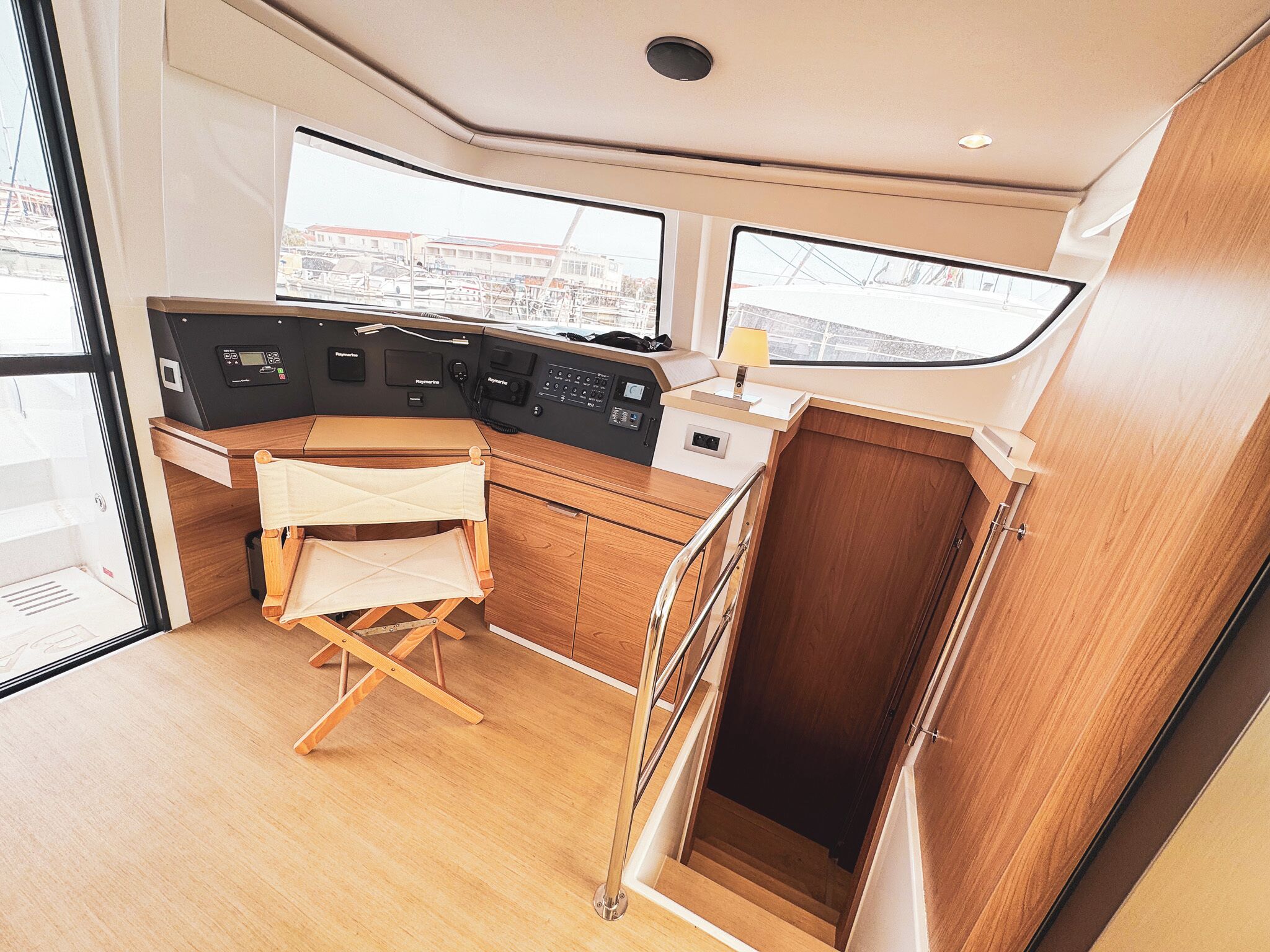 L'intérieur d'un bateau, avec un bureau en bois, des panneaux de contrôle et une vue à travers les fenêtres.