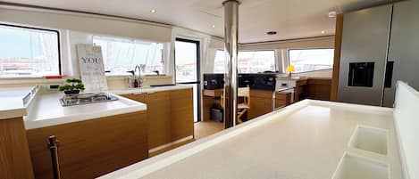 A modern kitchen with wooden cabinets, a central island, and a view of the city through large windows.