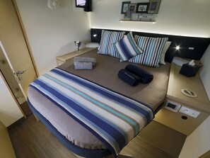 A neatly arranged bedroom with a bed, bedside tables, a nightstand, and a wall-mounted TV. - Sun-Kissed Sailing Adventure in Islas Sarónicas (Alimos)