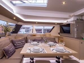 A yacht interior with a dining area, lounge seating, a TV, and a view of the harbor. - Sun-Kissed Sailing Adventure in Islas Sarónicas (Alimos)