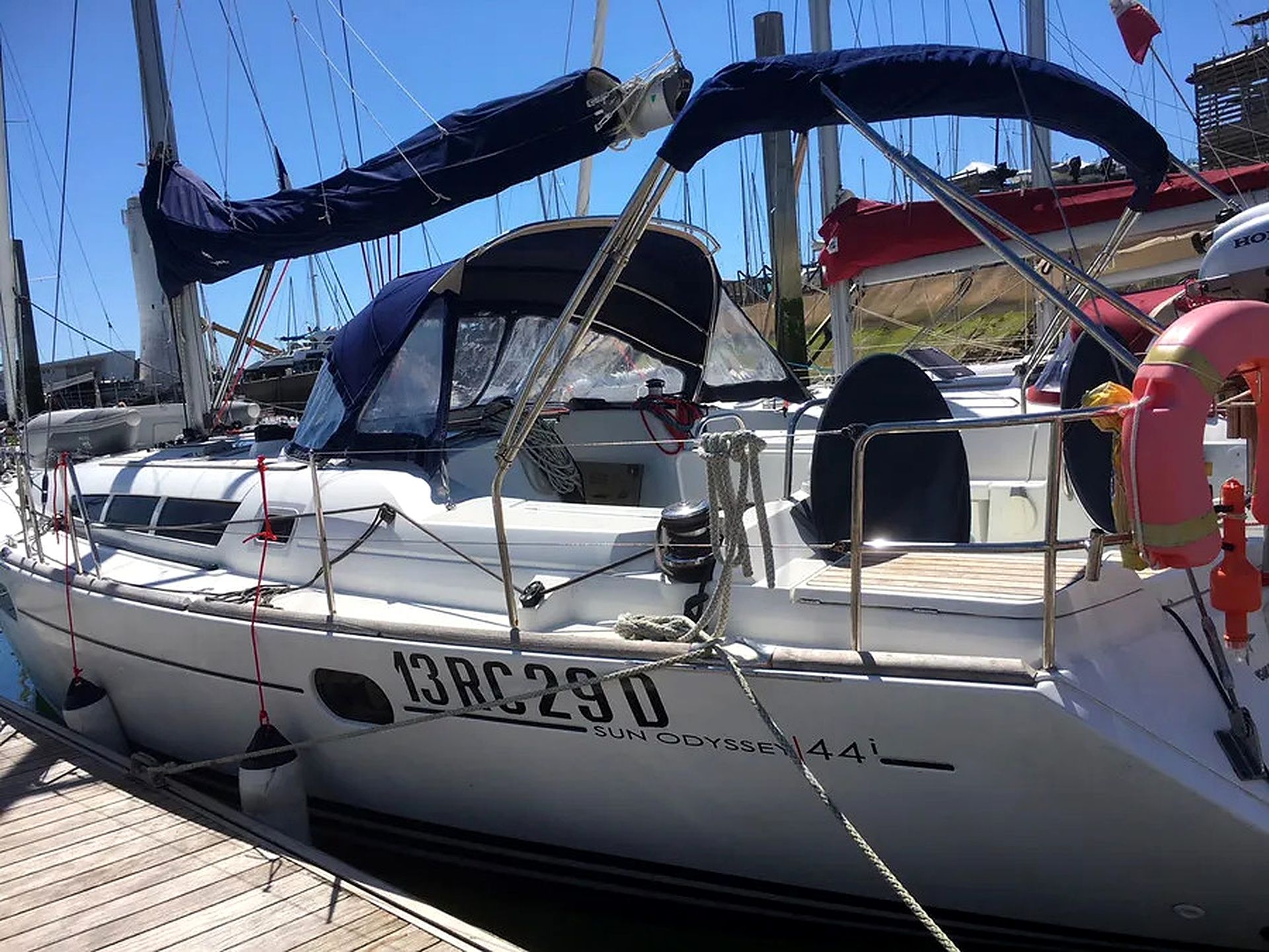 Un voilier est amarré dans une marina. On peut y voir une cabine, une bouée de sauvetage et le numéro « 13RC290 ».