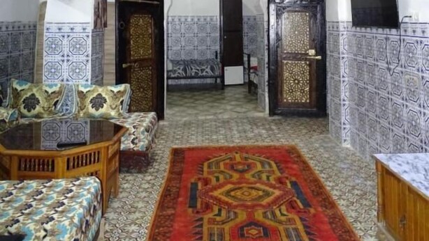 Um quarto com carpete estampado, um sofá, uma mesa de centro de madeira e uma televisão.