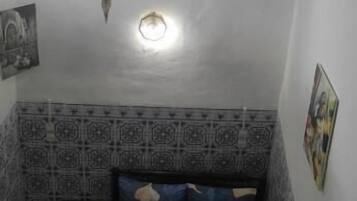 Una stanza piccola con un letto, un comodino, una mensola a parete e un lampadario.
