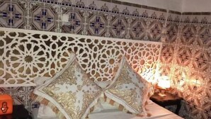 Quarto com cama, cabeceira estampada, almofadas, mesa de cabeceira e abajur.