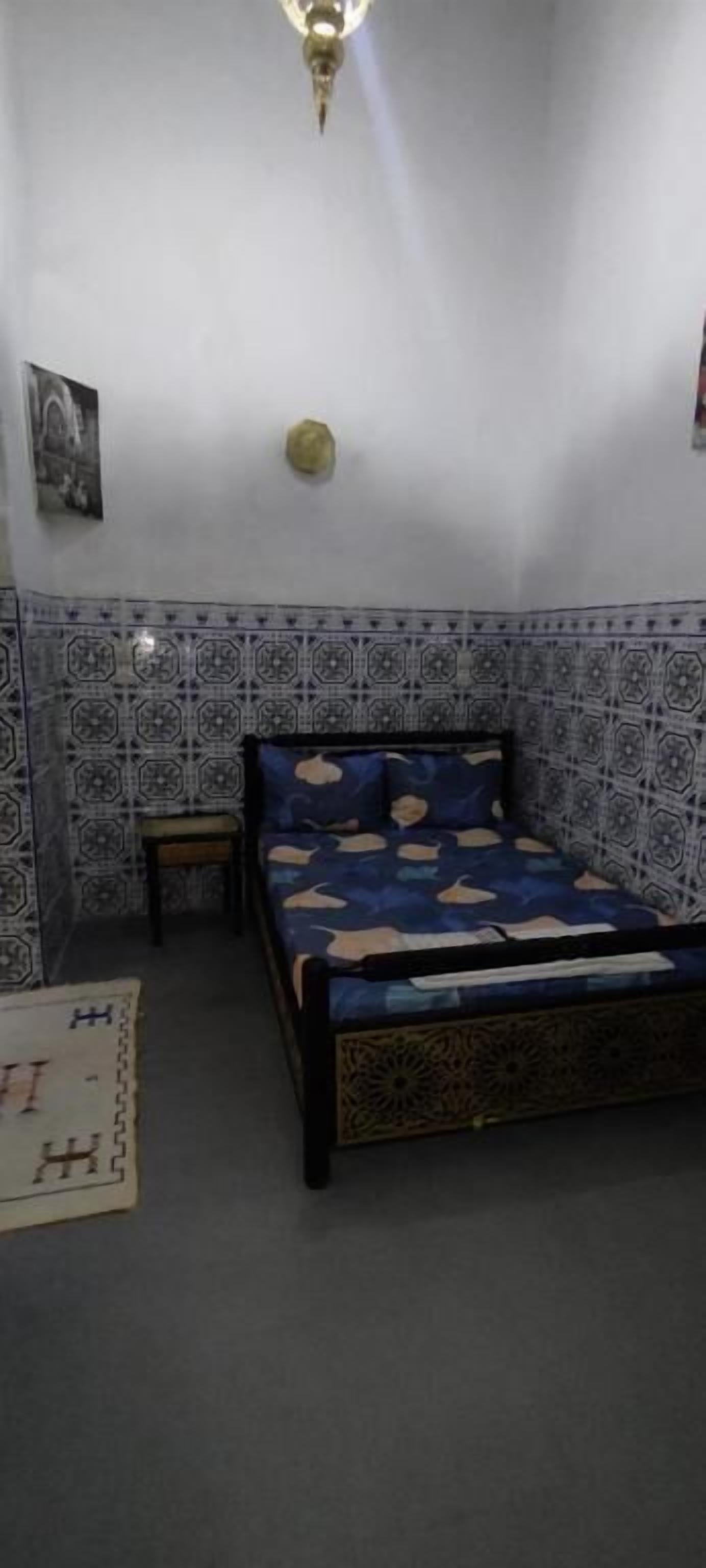 Quarto com uma cama, uma mesa de cabeceira pequena, luminária na parede e um papel de parede estampado.