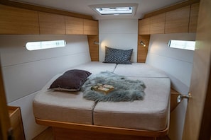 Ein kompakter Wohnraum in einem Wohnmobil mit Bett, Dachfenster und Holzausstattung.