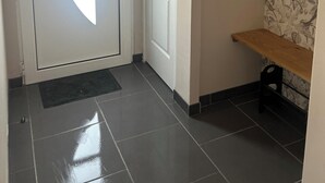 A hallway with a white door featuring a large window, a plain wall with a small shelf, and a tiled floor. - A bright vacation rental in the heart of the countryside, near the Baie de Somme (Vron)