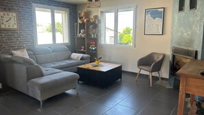 A living room with a grey sectional sofa, a coffee table, a grey armchair, a fireplace, and a brick wall. - A bright vacation rental in the heart of the countryside, near the Baie de Somme (Vron)