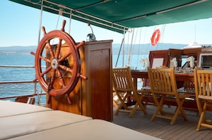 A deck with a wooden table and chairs, a steering wheel, and a lifebuoy.