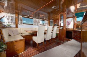 A boat interior with a wooden deck, cushioned seating, a dining area, and a control panel. - Sun-Kissed Sailing Adventure in Split-Dalmacia, Croatia (Jesenice)
