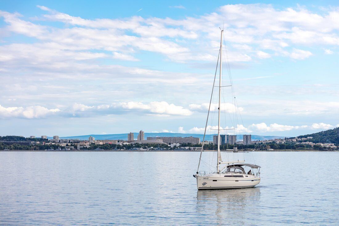 Ein Segelboot auf ruhigem Wasser, im Hintergrund eine Stadtansicht.