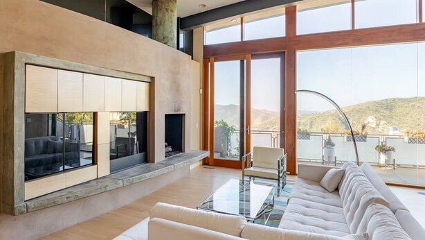 Una sala de estar moderna con chimenea, ventanas amplias y un balcón con vistas.