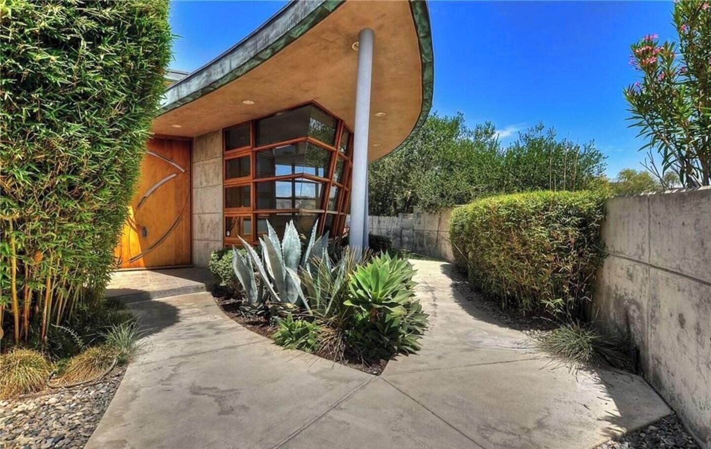 A modern building with a curved facade, a concrete pathway, and various plants.