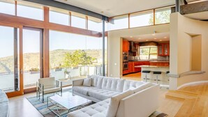 Una sala de estar moderna con un sofá, una mesa de centro de vidrio y vistas a una cocina y un balcón.
