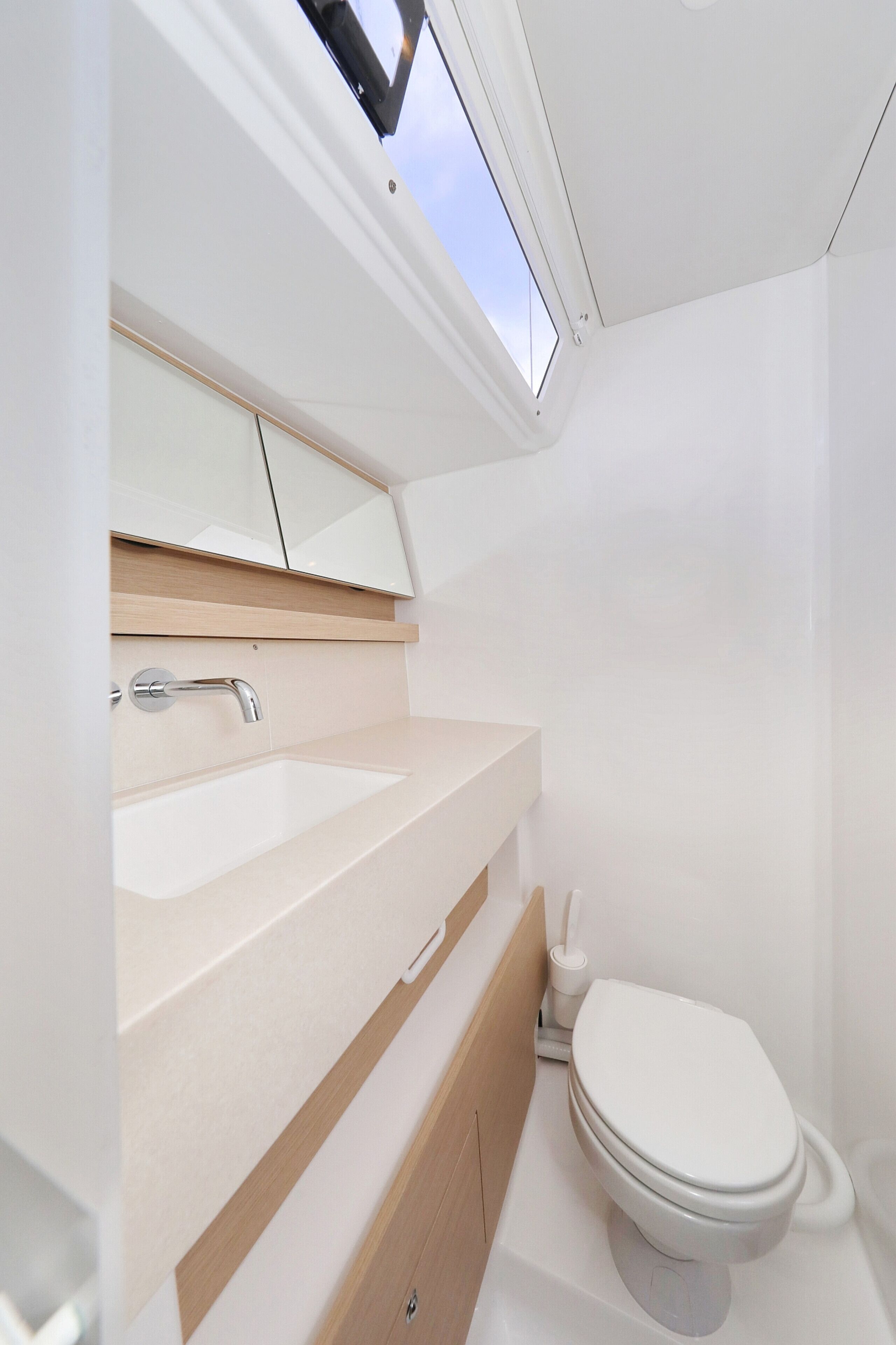 A modern bathroom with a skylight, a sink, a toilet, and wooden cabinetry.