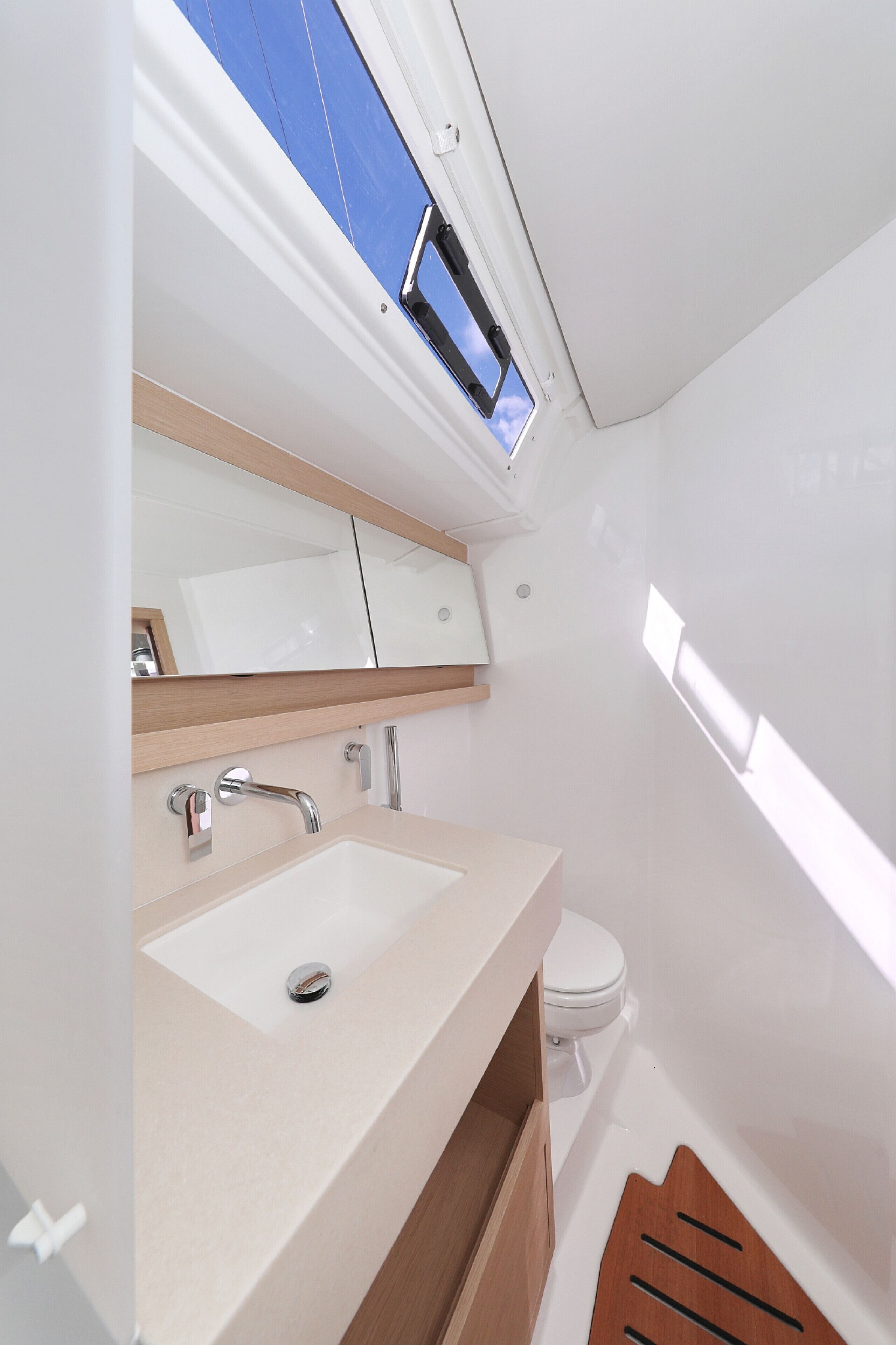 Une salle de bain moderne avec un lavabo blanc, un miroir et des toilettes, une lucarne au-dessus du lavabo et un meuble-lavabo en bois.