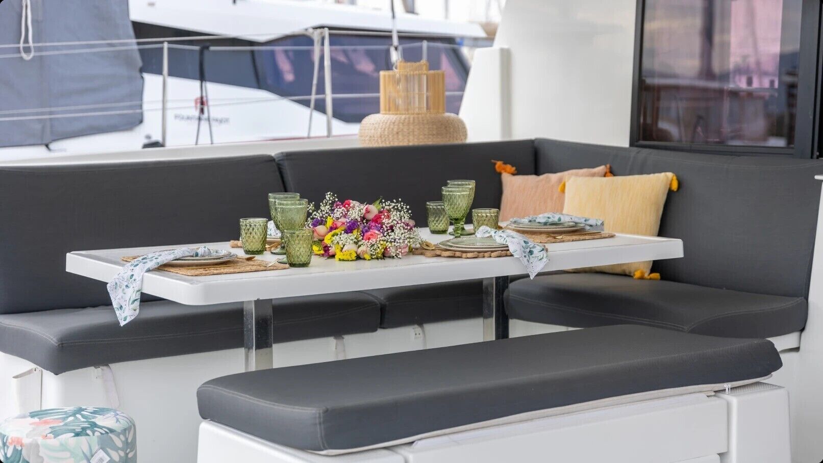 A boat interior with a dining table set for two, cushioned seating, and a decorative centerpiece.