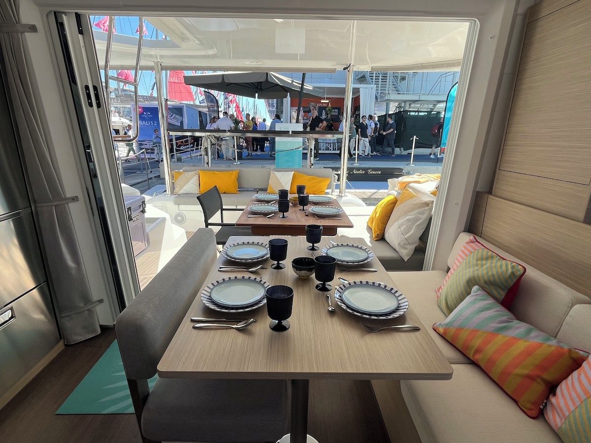 A dining area with tables set for four, a sofa with colorful cushions, and a view of an outdoor event.