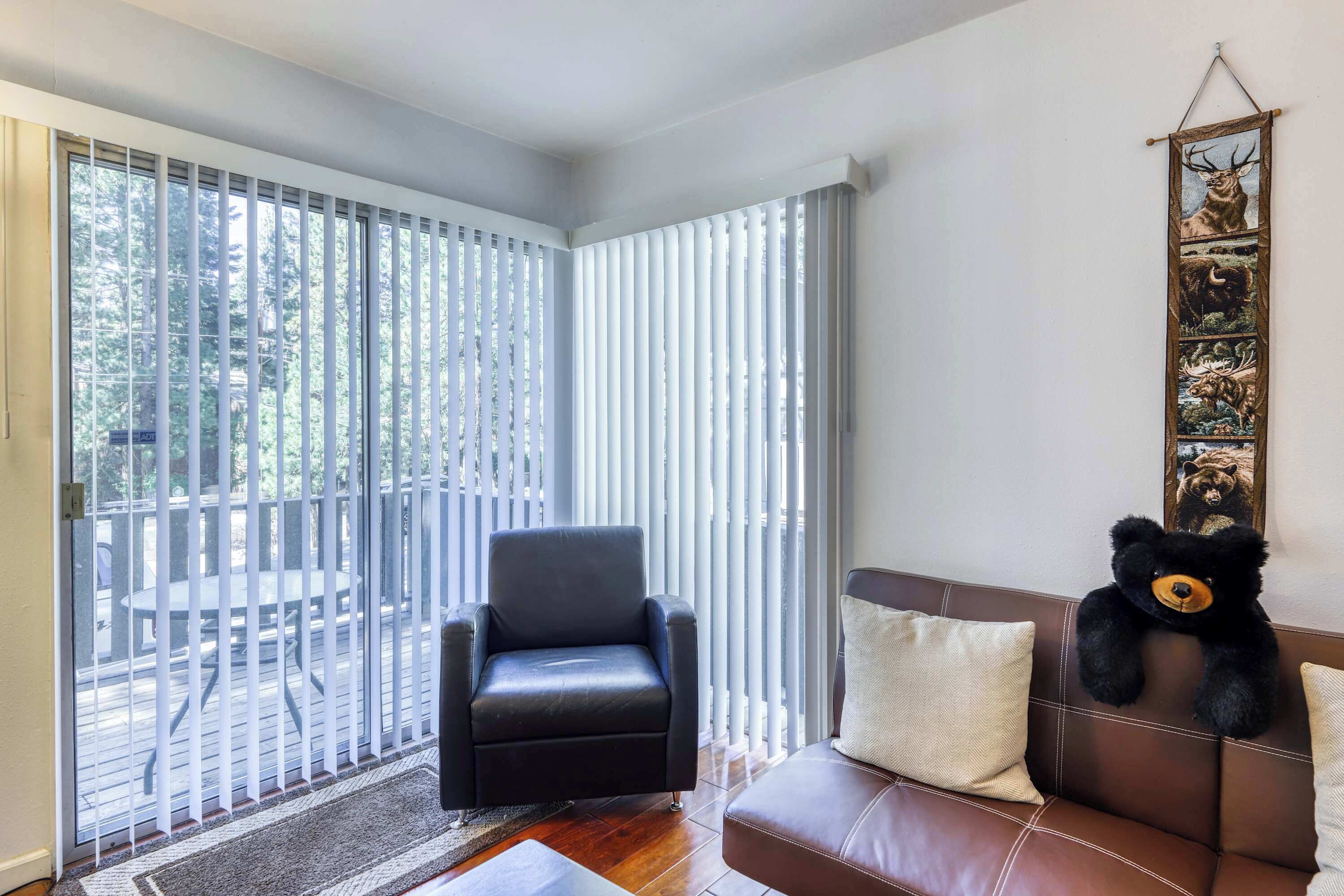 A room with a black leather chair, a brown leather sofa, a teddy bear, and a wall with a bear painting.