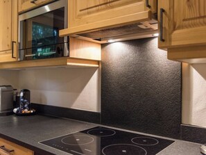 Une cuisine avec des meubles en bois, un four à micro-ondes en acier inoxydable et une plaque de cuisson à induction noire.