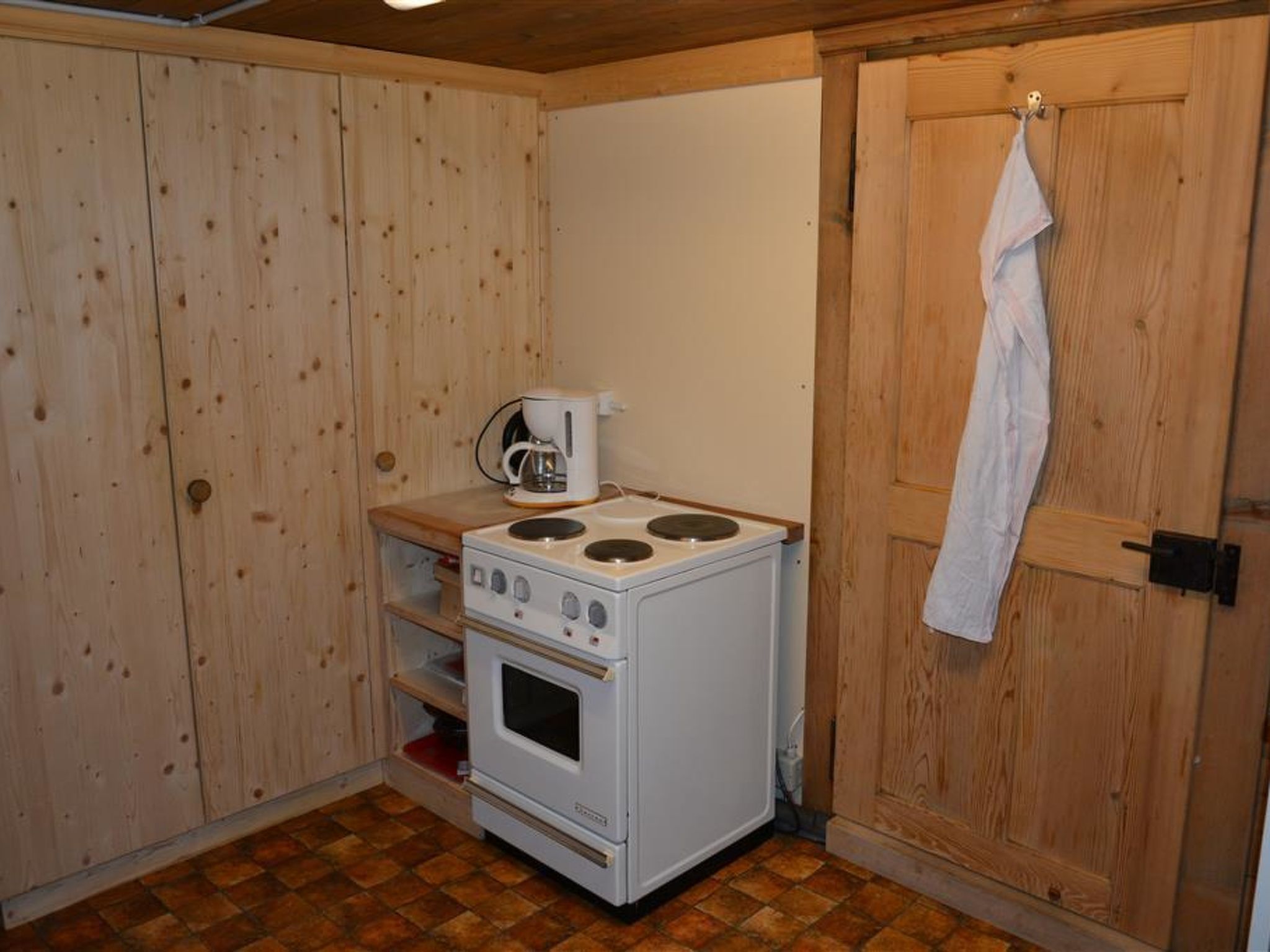 A compact kitchen with a white stove, a coffee maker, and wooden cabinets.