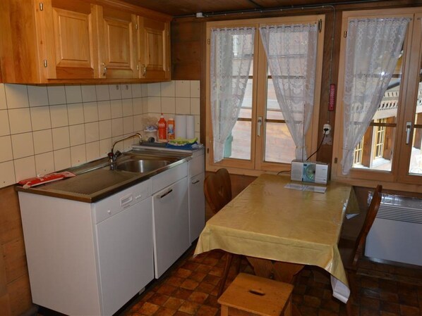 A compact kitchen with wooden cabinets, a built-in dishwasher, a sink, and a table with a tablecloth.