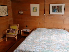 A wooden room with a bed, a chair, and a nightstand.
