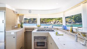 A compact kitchen with a gas stove, oven, and a large window overlooking a rocky coastline. - Sun-kissed Sailing Adventure in Split-Dalmatia, Croatia (Seget Donji)