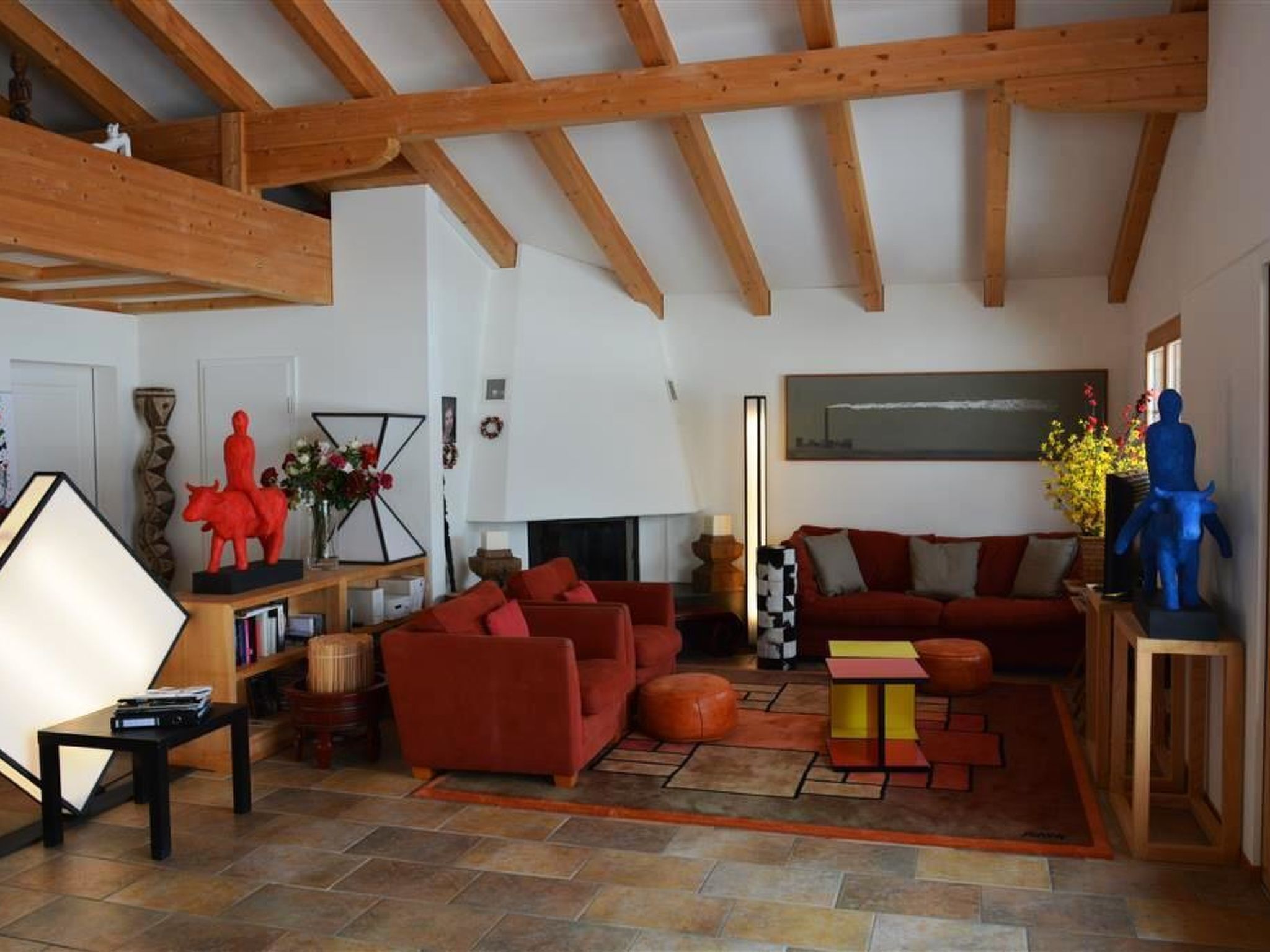 Ein geräumiges Wohnzimmer mit hoher Decke, Holzbalken, einem Kamin und moderner Einrichtung.