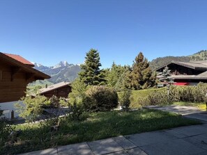 Eine Holzhütte mit Bergblick, umgeben von Grün und wolkenlosem Himmel.
