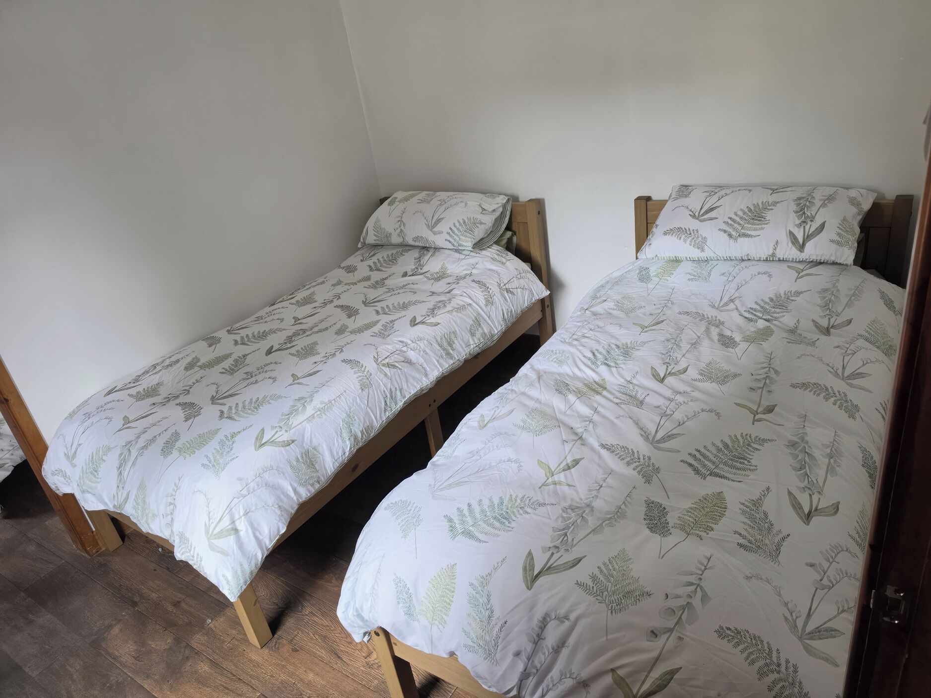 Dos camas individuales con cabeceros de madera y ropa de cama blanca con estampado de hojas.