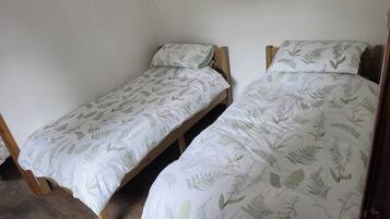 Dos camas individuales con cabeceros de madera y ropa de cama blanca con estampado de hojas.