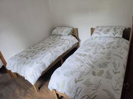 Dos camas individuales con cabeceros de madera y ropa de cama blanca con estampado de hojas.