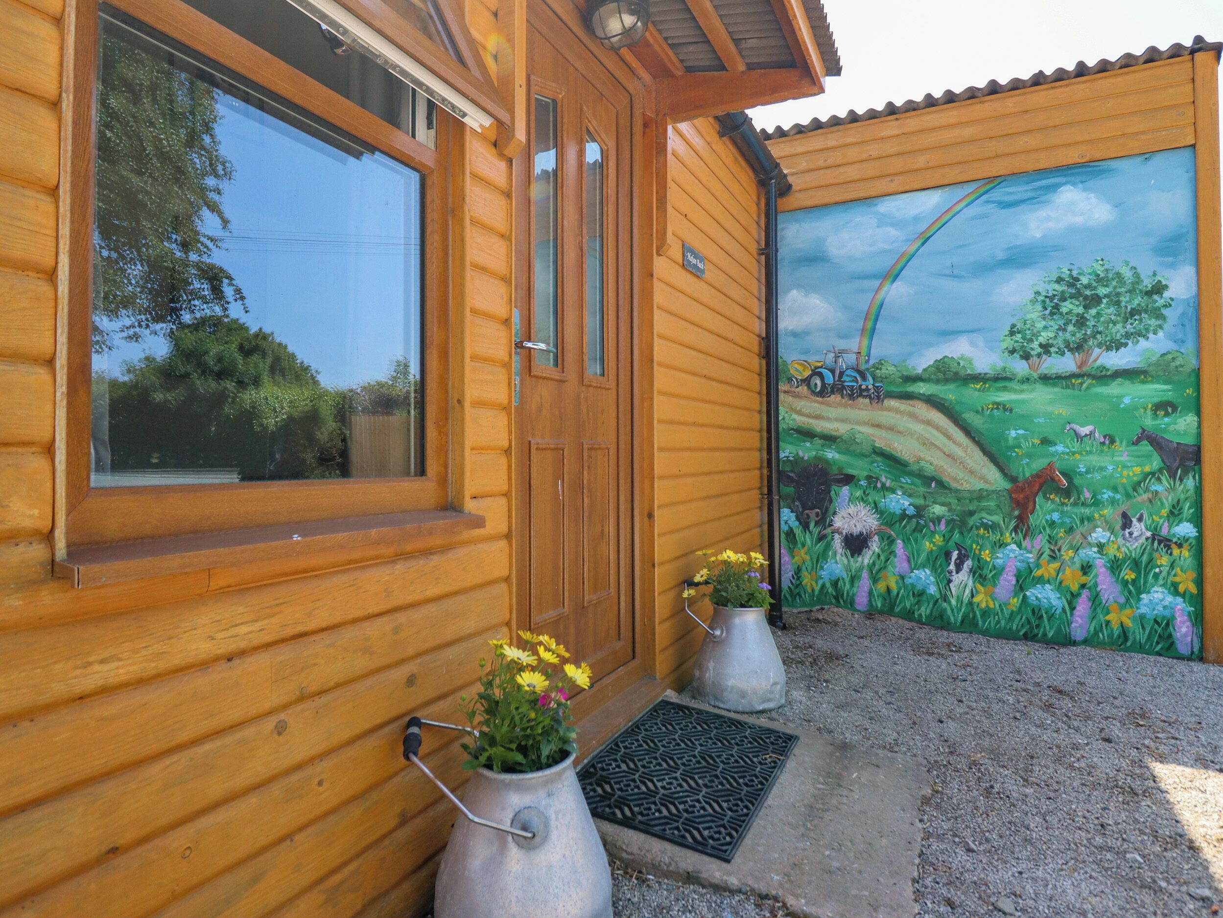 Uma cabana de madeira com porta, janelas e um mural representando uma cena rural.