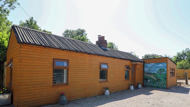 En træhytte med et bølgepapstag, skorsten og et muralmaleri på siden.