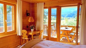 Eine Holzhütte mit einem Bett, einem Tisch mit Stühlen und Blick ins Freie.