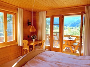 Eine Holzhütte mit einem Bett, einem Tisch mit Stühlen und Blick ins Freie.