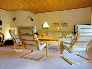 Een kamer met een houten plafond, een bank, twee schommelstoelen, een tafel en een lamp.
