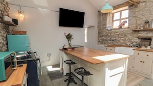 A kitchen with a wooden island, a stone wall, a teal refrigerator, and a mounted TV. - The Cottage at Thorpe Farm (York)