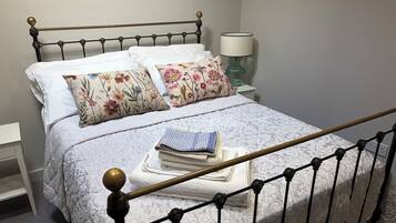 A neatly made bed with floral pillows, a lamp, and a bedside table with a folded towel.