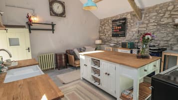 A kitchen with a wooden island, white cabinets, a stone wall, a clock, and a sign indicating a station.
